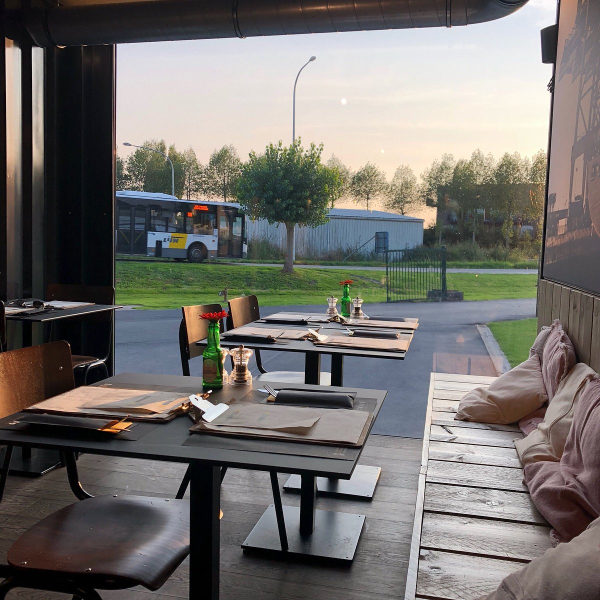 Gedekte tafels bij de open voorkant van de container, met zicht op de bomen en de straat.