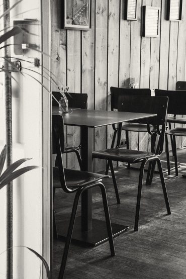 Zwarte stoelen en een tafel tegen een houten wand, in zwart-wit.